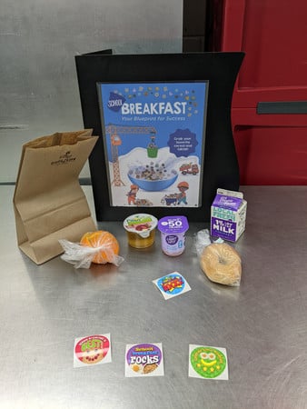 School breakfast program with milk, bagel, fruit, yogurt, apple juice and stickers