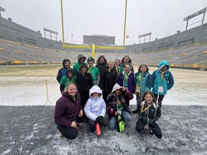 A group of students pose together at Lambeau Field on a windy, snowy day
